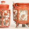 Een lot van twee Japans porseleinen potjes. Rood gekleurd met vergulde details en met illustraties en gedragen door figuren. Het kleinere met deksel en onderdeksel. Omstreeks 1900.
