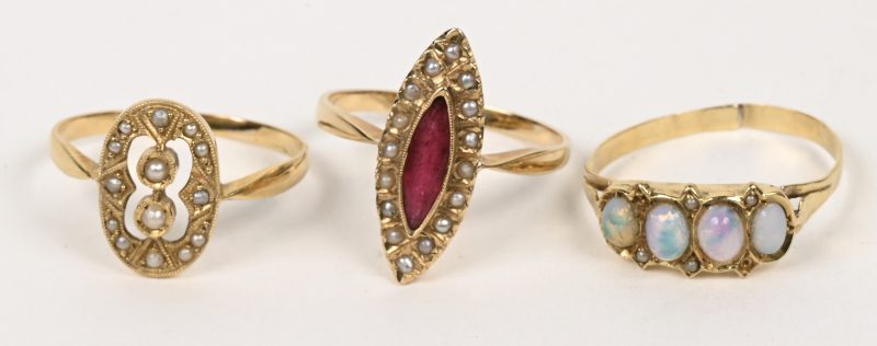 Drie verschillende 18 karaats geelgouden ringen bezet met pareltjes, opaal en een rode steen.