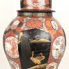 Een Imari porseleinen vaas met toegevoegde decoratie van gouden vogels op zwarte achtergrond. Fo-hond op deksel zwaar beschadigd. Onderaan gemerkt.