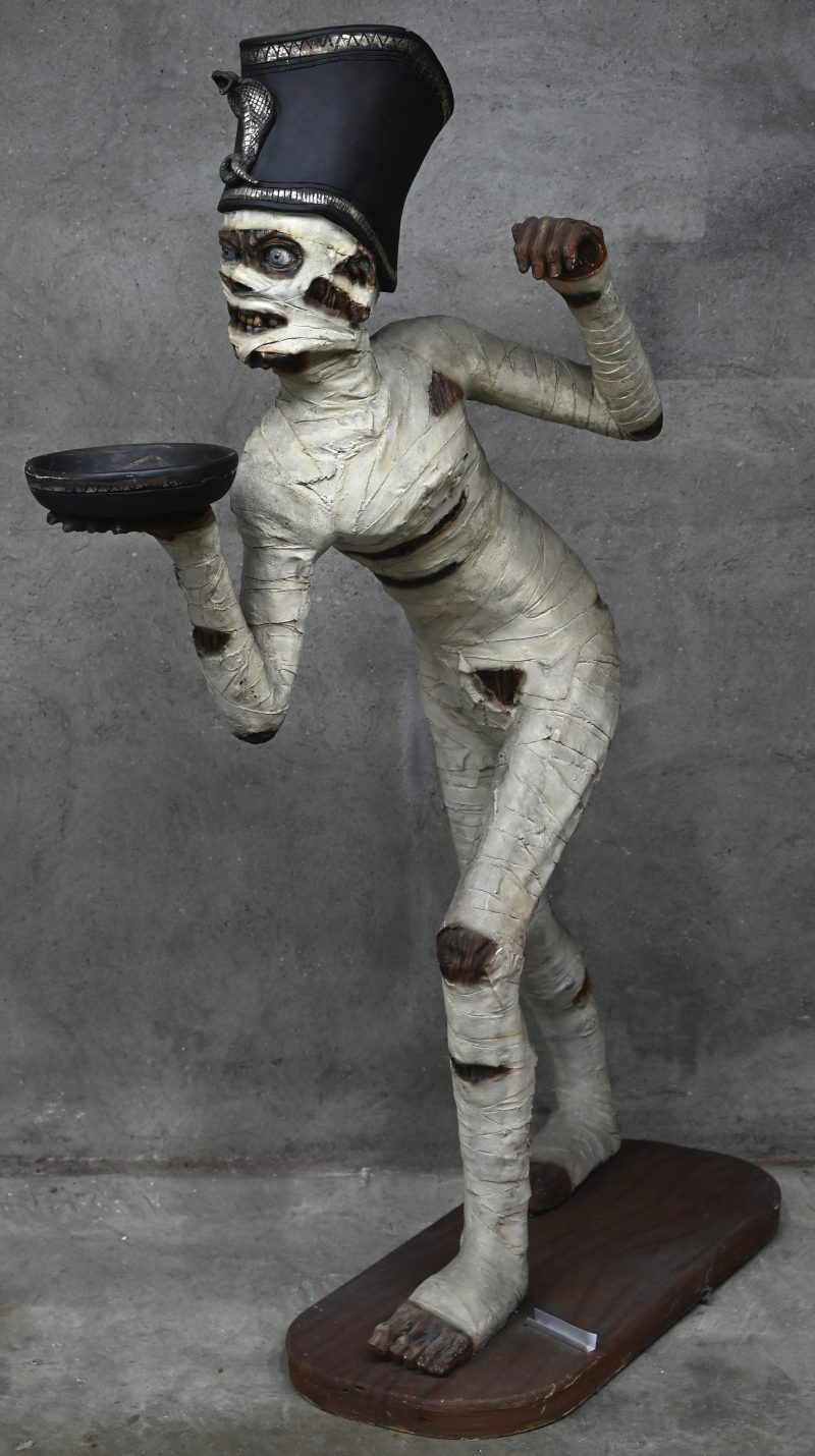 Een beeld van polyester, met voorstelling van een wandelende mummie met een dienblad.