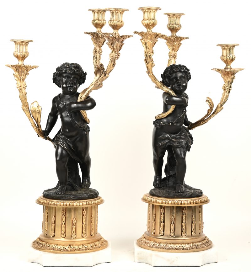 lot van 2 bronzen Cupido kandelaren  met 3 vergulde lichtpunten, op messing sokkel en wit-marmeren voetstuk
