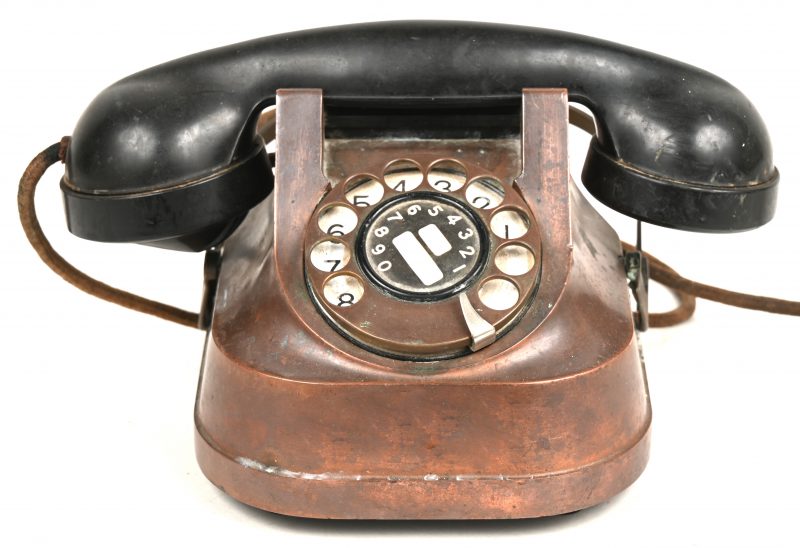 Een oude roodkoperen draaischijftelefoon met bakelieten hoorn.