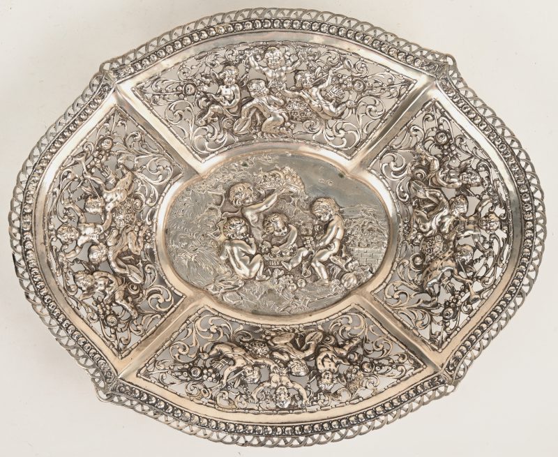 Een ovale gedreven zilveren siermandje met deels ajour decor van oogsten putti. Gemerkt en gehaltekeur 800/1000.