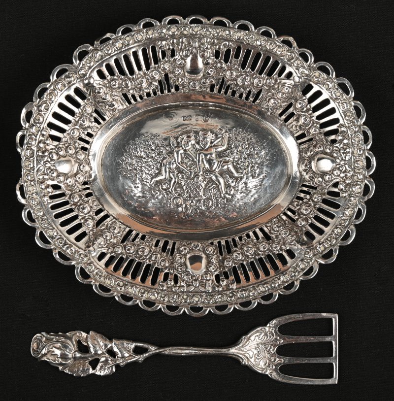 Een zilveren schaaltje met schep, meet decoratie van een Bachanaal tafereel.