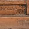 Een bronzen, gesculptuurd beeldje van een dronkaard op stoel met opschrift vooraan “OP-SIGNOOR!!”. Achteraan “K. Denckens 1943”, vermoedelijk aandenken, gericht aan Koninklijke Postzegelkring Karel Denckens Mechelen, gesigneerd door “G Hendrickx Ciseleur”.