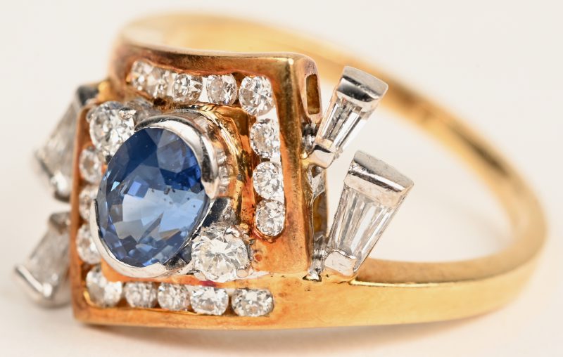 Een 18 karaats wit en geelgouden ring bezet met een centrale saffier van +- 1 ct. en briljanten en diamant baguetten met een gezamenlijk gewicht van +- 1 ct.