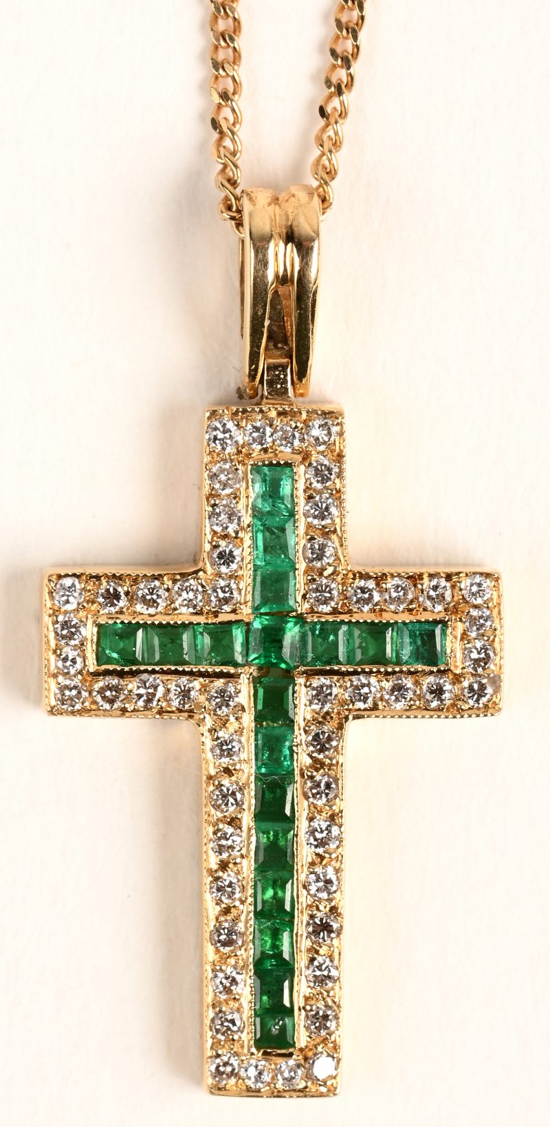 Een 18 karaats geelgouden ketting met henger in de vorm van een kruis bezet met gekalibreerde smaragden met een gezamenlijk gewicht van +- 0,30 ct. en briljanten met een gezamenlijk gewicht van +- 0,25 ct.
