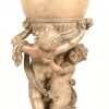 Een grijsgeschilderde aardewerken vaas gedragen door twee puto’s. Slijtage en randschade onderaan.