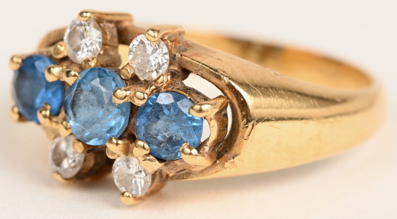 Een 18 karaats geelgouden ring bezet met drie saffieren met een gezamenlijk gewicht van +- 0,60 ct. en vier diamanten met een gezamenlijk gewicht van +- 0,20 ct.