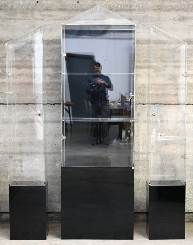 Een set van drie afsluitbare plexiglazen design vitrines op zwarte staanders. Telkens met 2 niveaus.