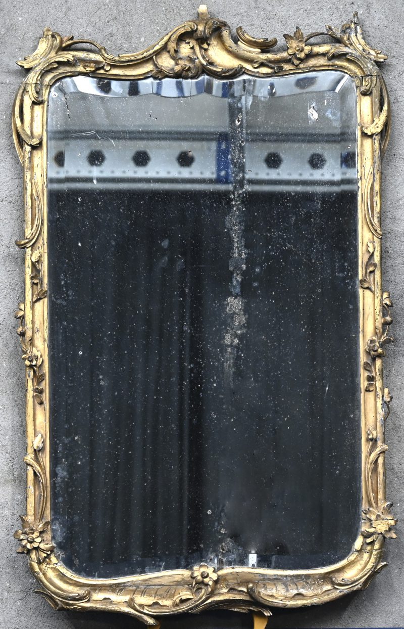 Een Italiaanse spiegel met gesneden en verguld houten lijst en met gebosseerd glas. Gebruikssporen. Omstreeks 1800.