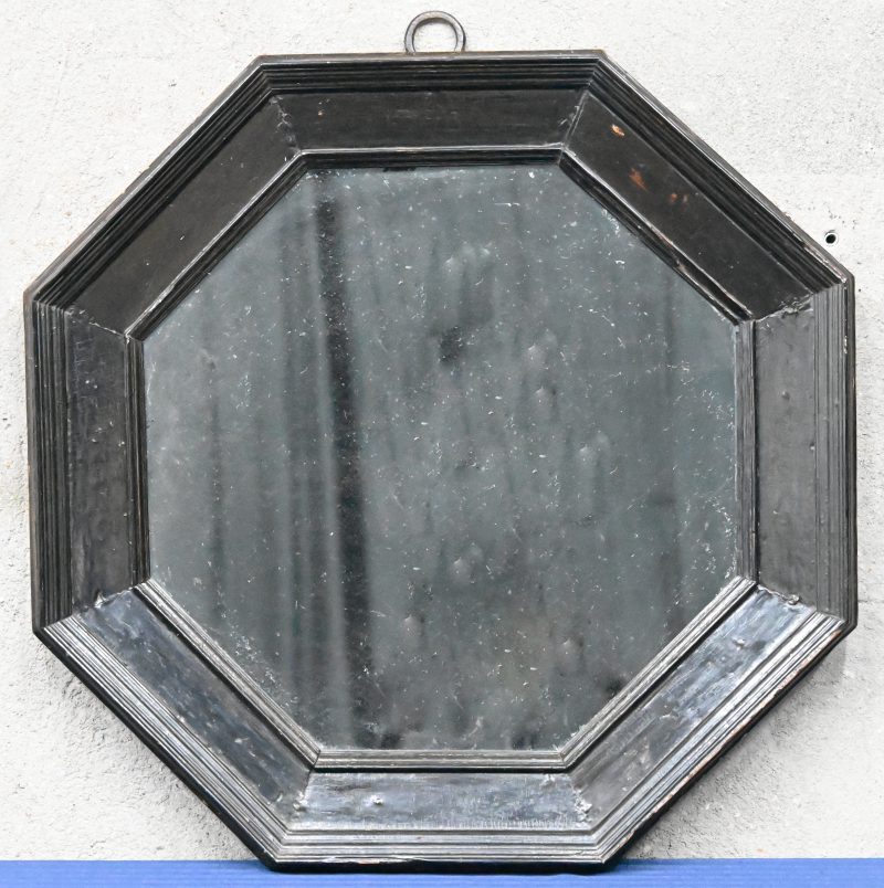 Achthoekige spiegel met zwarte houten lijst.