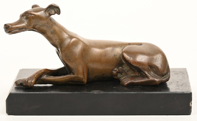 Een bronzen hondje, liggende op een marmeren sokkel.
