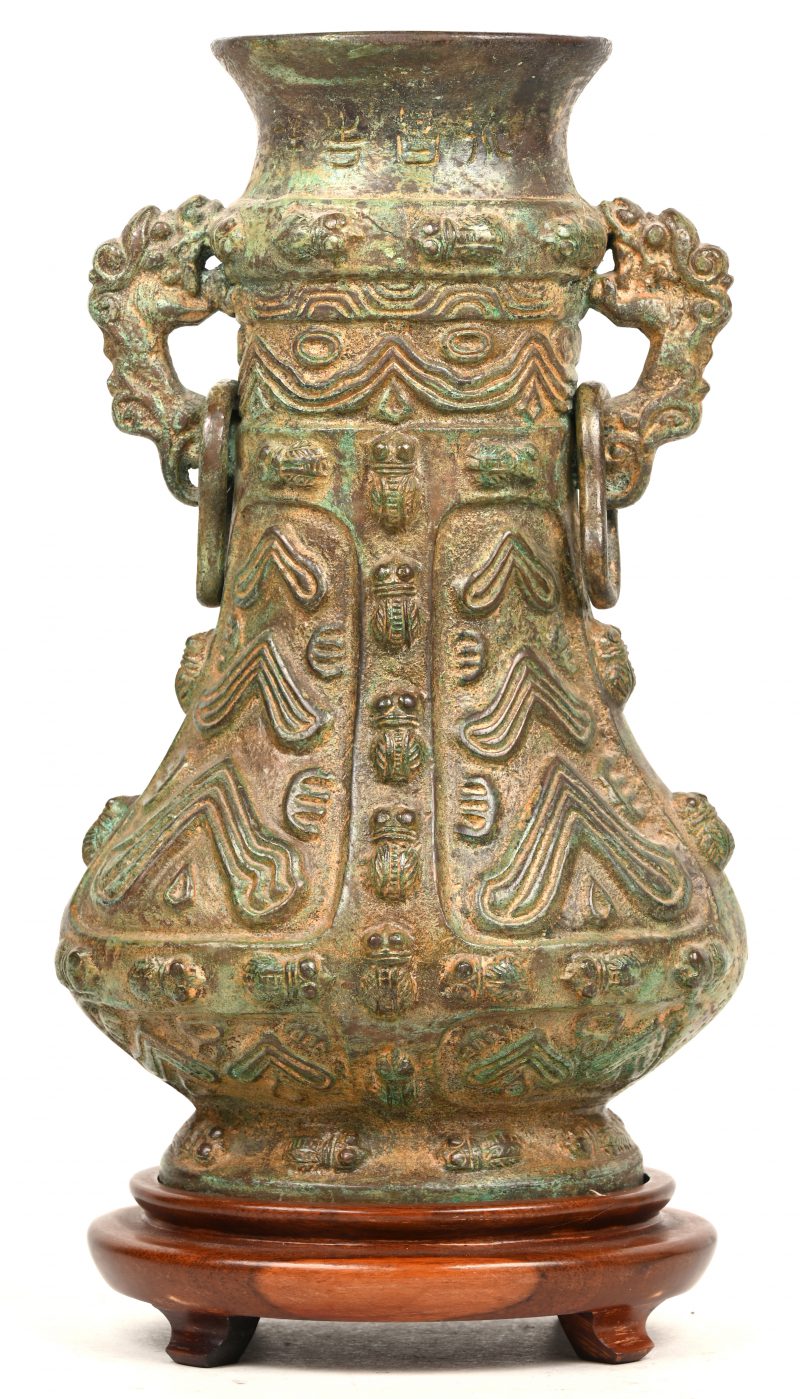 Een Chinees brons gesculpteerde “Zun” vaas. Op houten sokkel, met diverse sculpturen afgebeeld en drakenhoofden als oren.