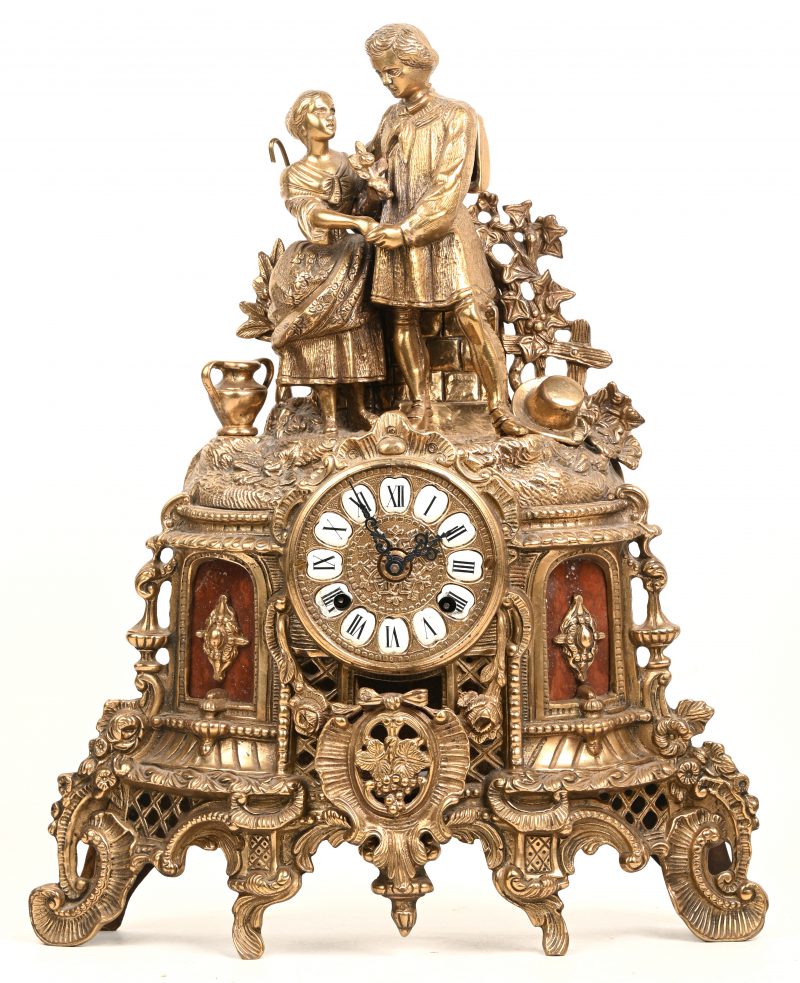 Een bronzen Italiaanse Imperial klok, binnenin gemarkeerd “Brevettato”. FHS Germany uurwerk met dubbele belslag. Divers gesculpteerd reliëf met bovenaan koppel in omhelzing. Vermoedelijk kunstgieterij “Fonderia Artistica”.
