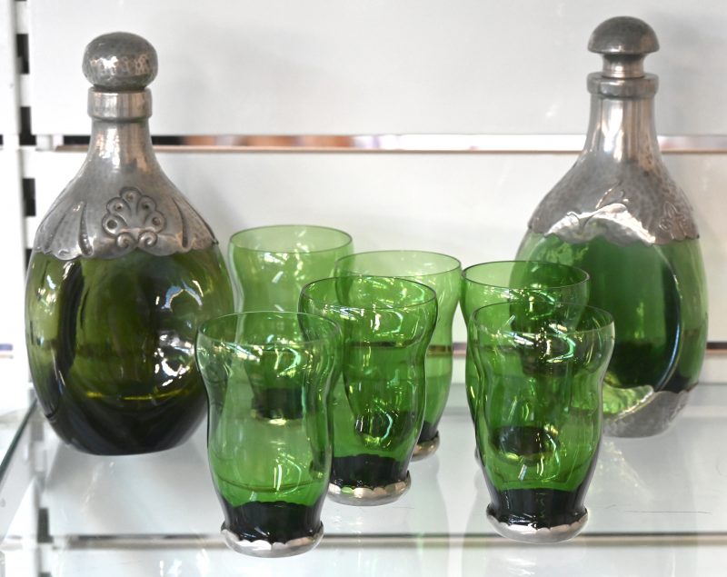 Een set bestaande uit zes groene glazen met tinnen voet en twee karaffen met tinnen beslag en stop. Onderaan gemerkt.