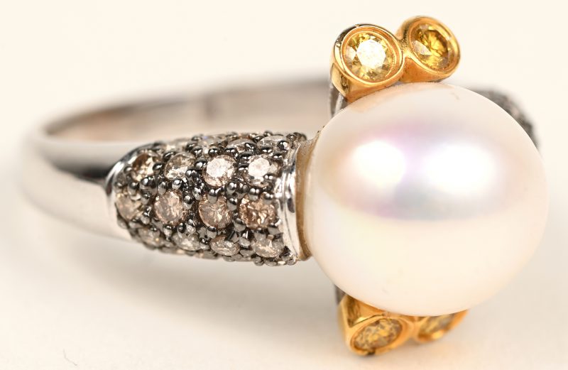 Een 18 karaats wit en geelgouden ring bezet met briljanten witte en gele met een gezamenlijk gewicht van +- 0,76 ct. en een parel.