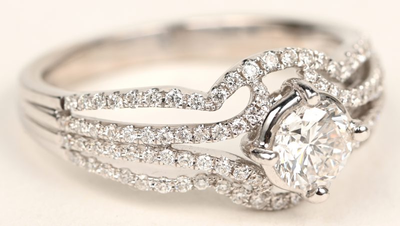 Een 18 karaats witgouden ring bezet met een centrale diamant van +- 0,56 ct. FSI2. en briljanten met een gezamenlijk gewicht van +- 0,40 ct FVS1.