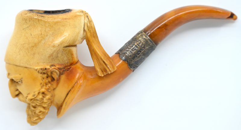 Een pijp met pijpenkop van gebeeldhouwd meerschuim in de vorm van een Ulaan met baard en muts. Korte amberen, afgebeten steel.