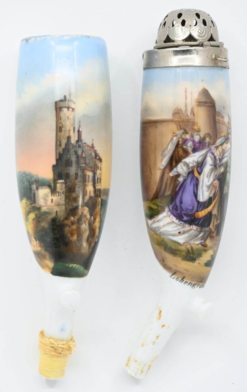 Twee porseleinen pijpenkoppen, de ene versierd met een kasteel, de andere met een historische scène, welke een metalen deksel heeft.