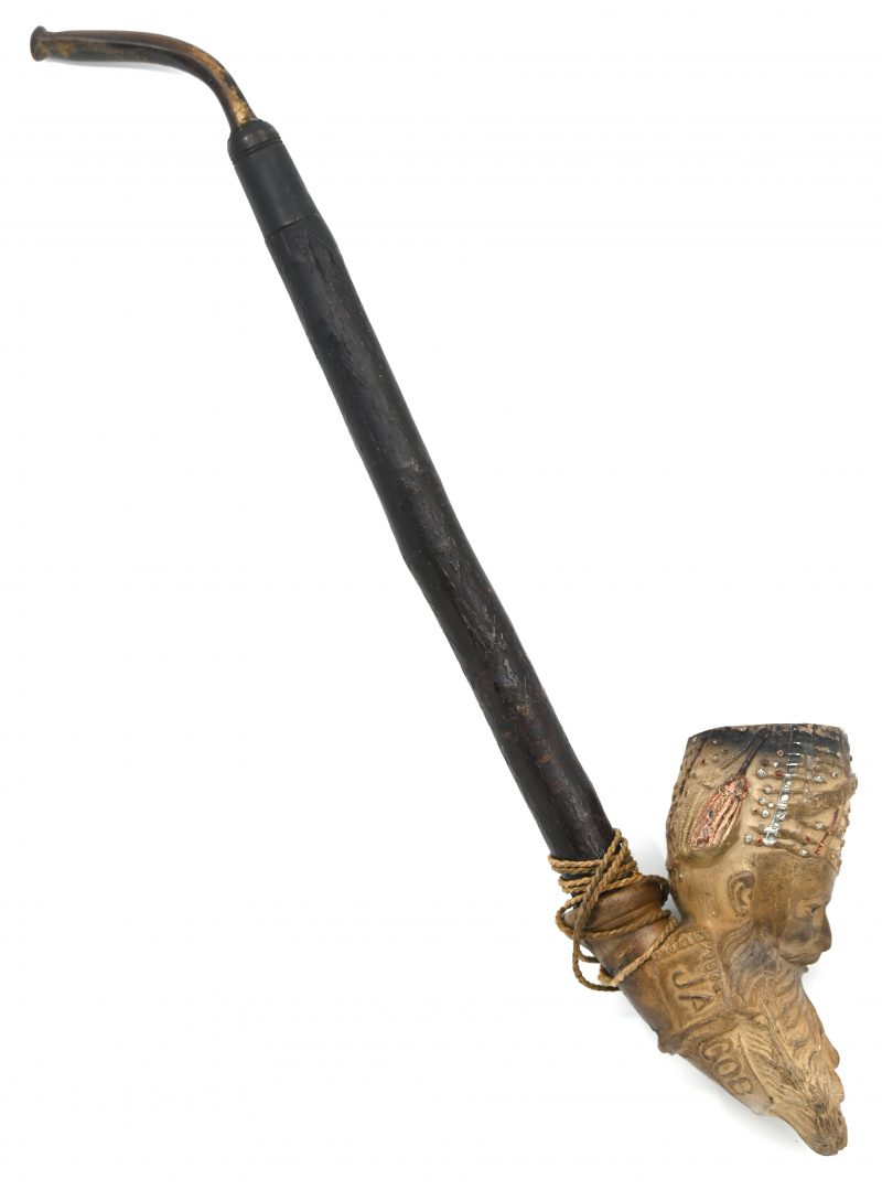 Een pijp met een pijpaarde kop in de vorm van een man met tulband en lange baard. Deels gekleurd en met opschrift Jacob. Berkenhouten steel en benen mondstuk.