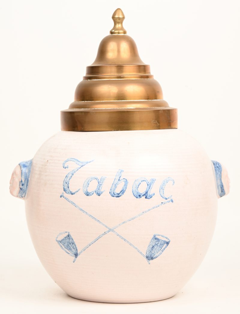 Een tabakspot van aardewerk met blauw opschrift “Tabac” boven twee blauwe geschilderde, gekruiste pijpen. Kegelvormig koperen deksel.