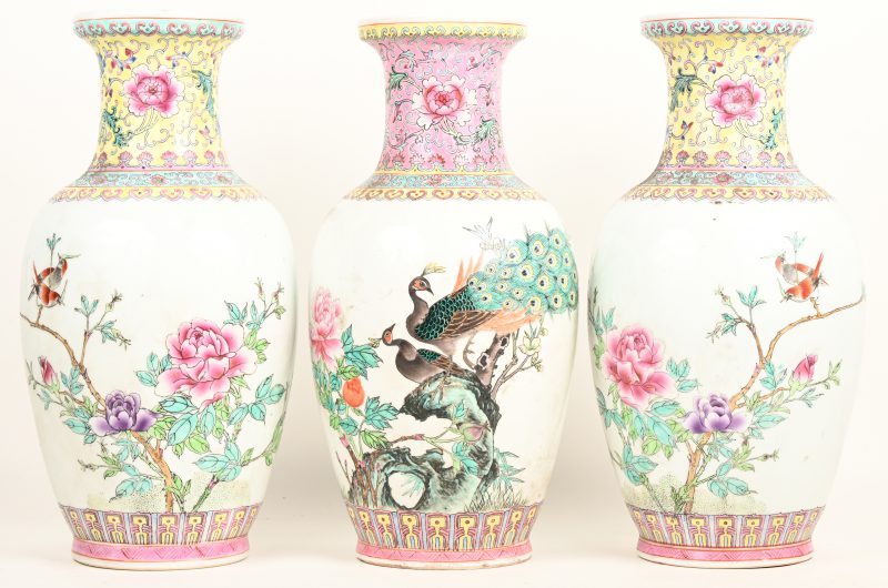 Een lot van drie Chinees porseleinen vazen, waarvan een paar met famille jaune decor en bloemen en vogels, en de andere met famille rose decor met pauwen. Onderaan gemerkt met stempel en ‘made in China’.