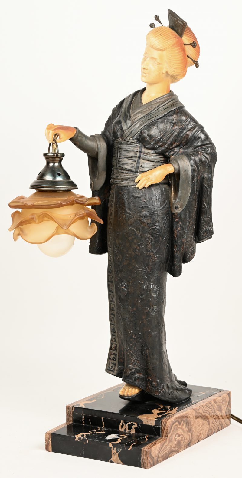 “Japonaise”. Een tafellamp uit zamak en kunstof op marmeren voet. Afgebeeld een Japanse Geisha met lantaarn. Onderaan gesigneerd “Alonzo”.