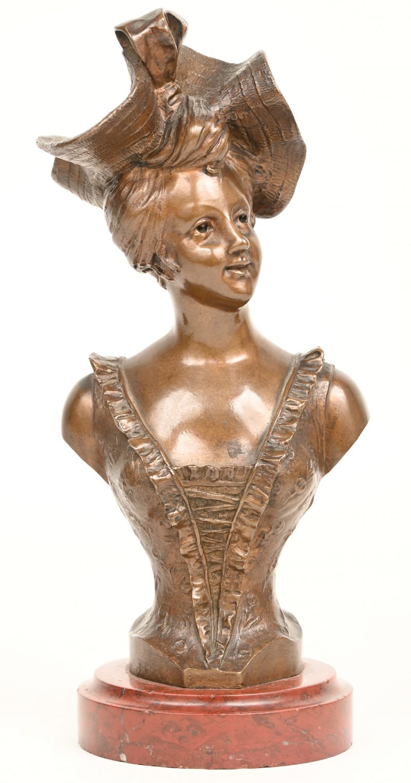 “Buste van een dame met hoed”. Een brons gepatineerd borstbeeld van een dame met hoed op een marmeren voet. Gesigneerd “Alphonse Piquemal”.