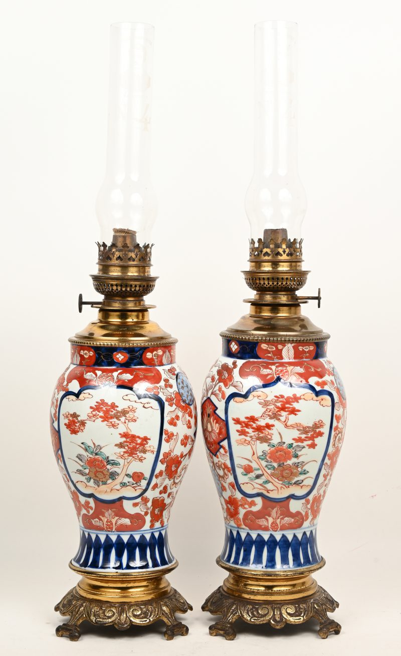 Een lot van 2 porseleinen olielampen met vergulde voet en lonthouder. Opzetglas gemerkt “Véritable Lampe Royal Farenthold No4”.