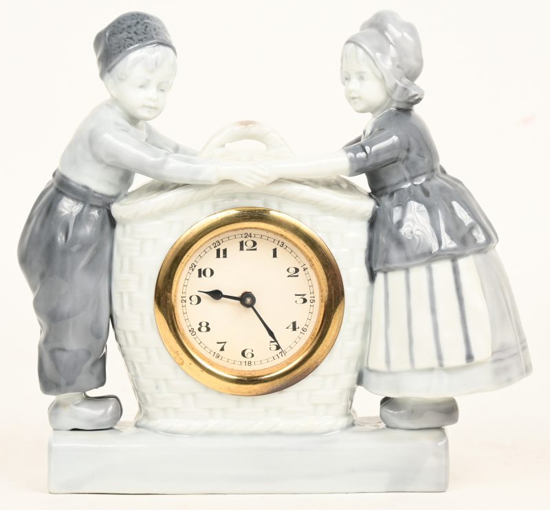 Een vintage porseleinen klokje met jongen en meisje versierd.
