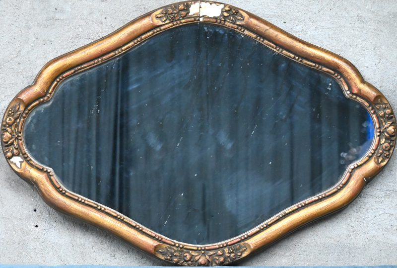 Een ovale spiegel in vergulde houten lijst. Schade aan de lijst.