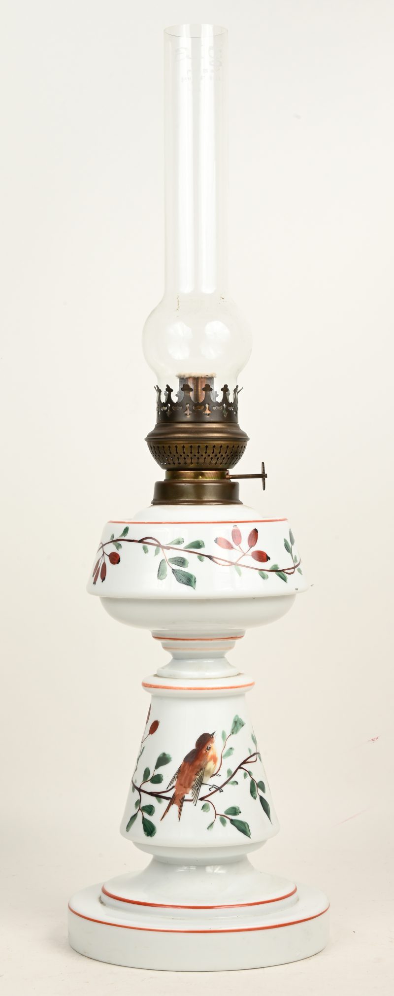 Een vintage porseleinen olielamp met witte body en handgeschilderd decor van een vogel op een tak. Lampglas gemerkt aig.