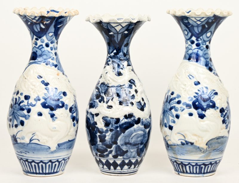 Drie diverse kraagvazen van Chinees blauw en wit porselein met een drakendecor in reliëf.  Eén beschadigd aan de rand.