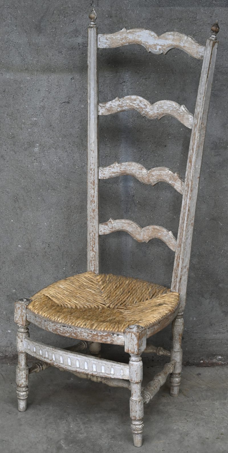 Een grijsgepatineerde houten kerkstoel met hoge rug en rieten zit.