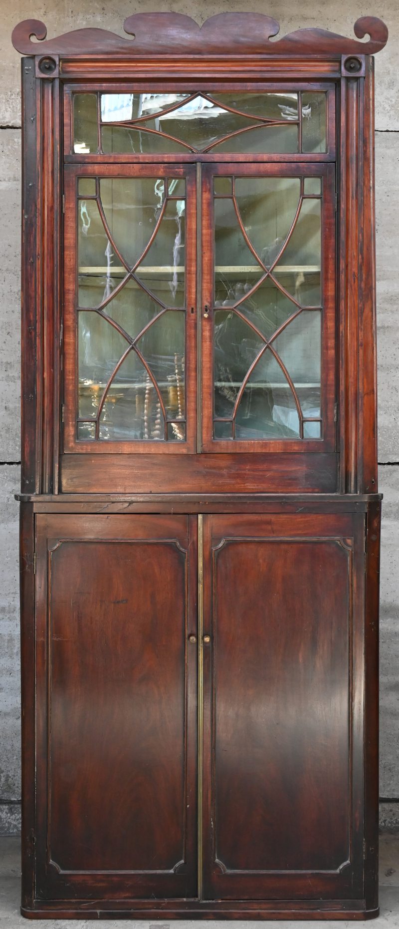 Een Georgian hoekbibliotheek van mahoniehout. Bovenaan twee beglaasde deuren met latwerk (twee ruitjes gebarsten), onderaan twee paneeldeuren. Messingen aanslaglijsten en uitgewerkte kroonlijst. XIXde eeuw.