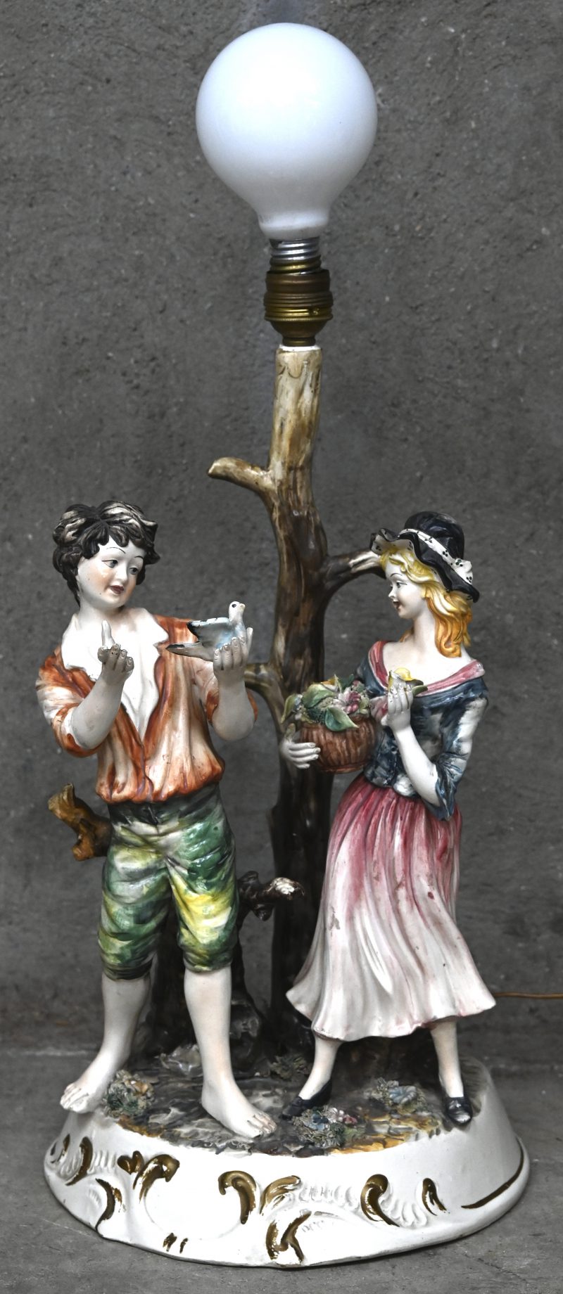 Een Capo di Monte lamp met beeld van jongen en meisje.
