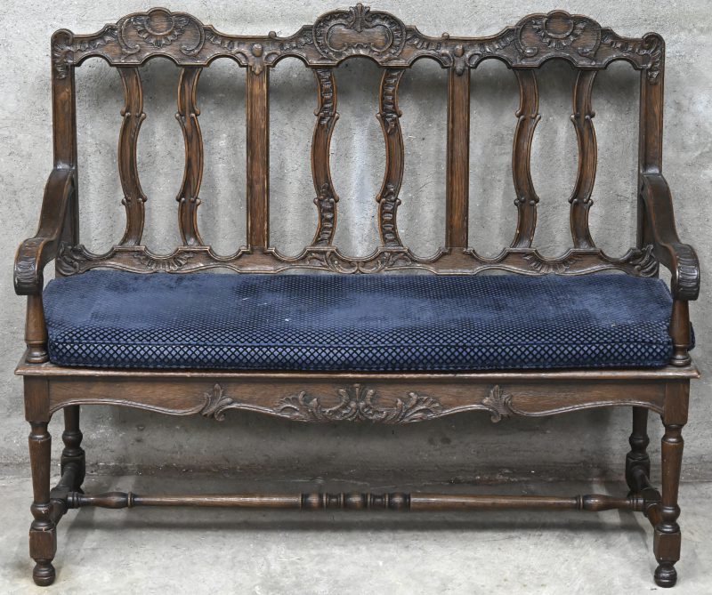 Een gesculpteerd houten zitbankje met blauw kussenzitting.