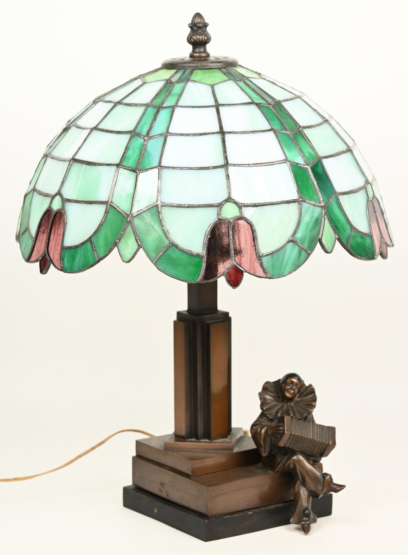 Een Tiffany tafellamp in de art-deco stijl met een pierrot met accordeon op de voet.