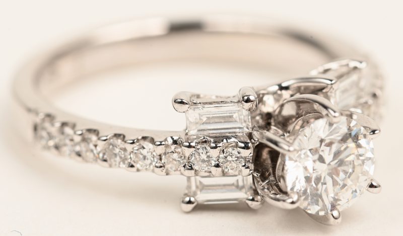 Een 18 karaats witgouden ring bezet een centrale briljant van +- 0,58 ct en  met een briljanten en twee diamant baguetten met een gezamenlijk gewicht van +- 0,56 ct.