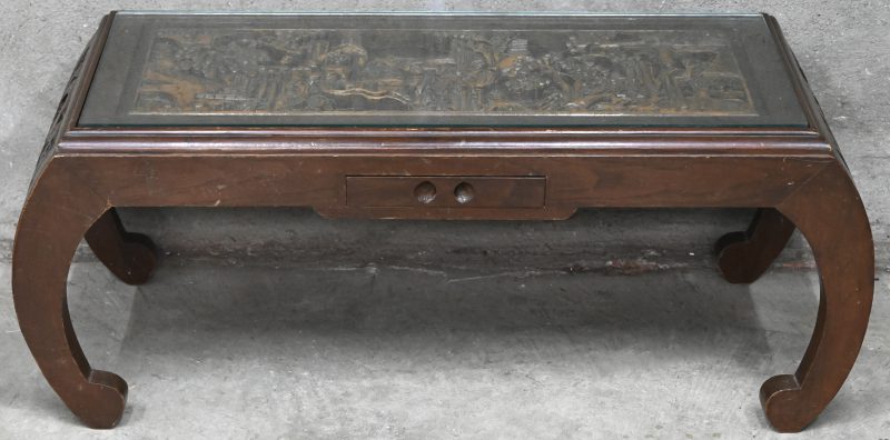 Een salontafel in hout met een Chinese relief decor , 1 lade en glazen blad.