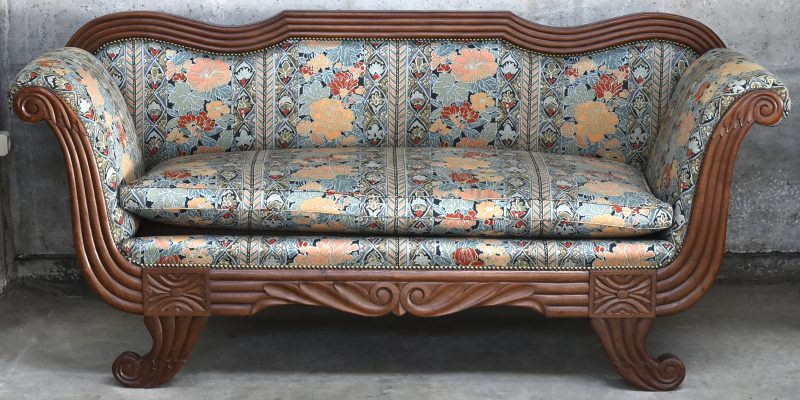 Een houten sofa met gesculpteerd frame en stoffering in bloemenmotief.