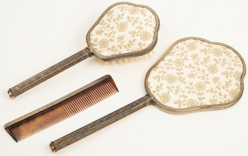 Een oude make-up set bestaande uit een spiegel, borstel en een kam.