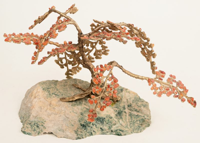 Een Bonzai boompje in kunstbrons met steentjes als bladeren op groenig gesteente.