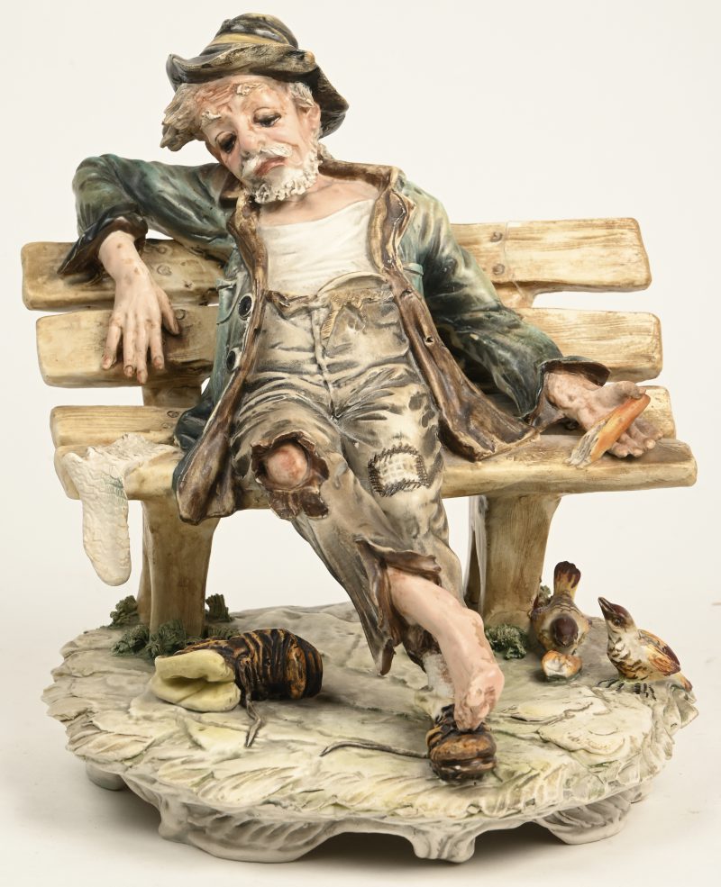 Een Capodimonte porseleinen beeldje van een landloper op een bankje. Restauratieschade thv het bankje.