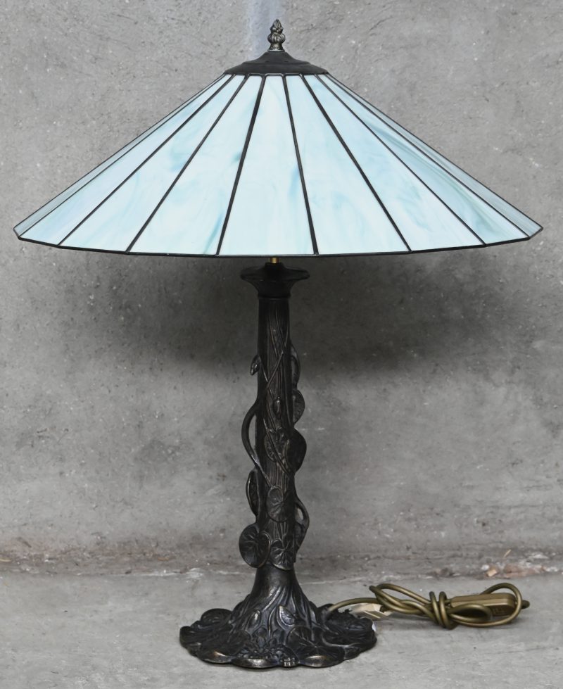 Een Tiffany tafellamp met bronskleurige voet in floraal motief en kap met groen glas.