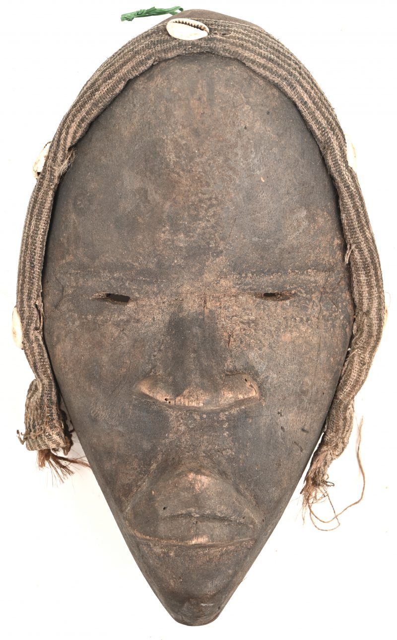Een hout gesculptuurd Afrikaans masker met textiel en kauri schelpjes versierd. Dan, Ivoorkust.