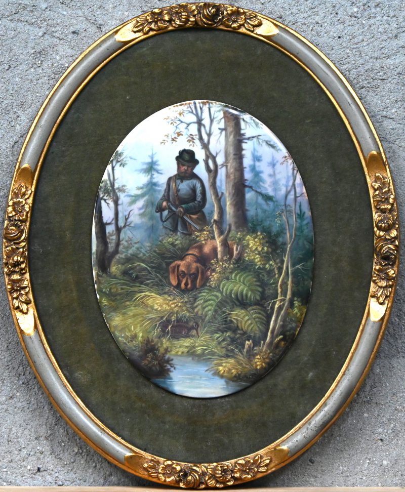 “Jager met hond”. Een porselein ovalen plaquette met vilten bekleding en vergulde kader. Frankrijk anno 1900.