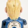 “Donald Trump”. Een aardewerken beeldje dat hand naar mond brengt, met opschrift achteraan “Make America Great Again”.