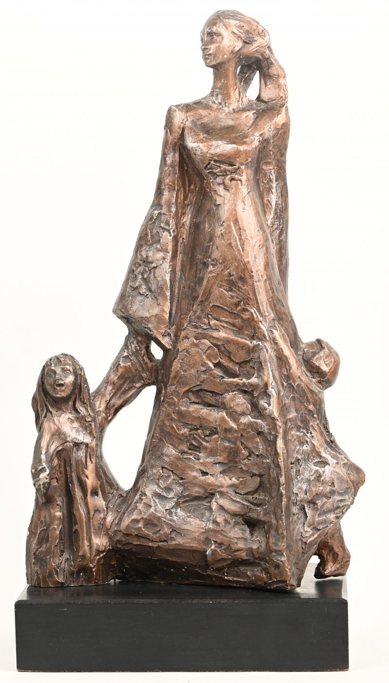 Een keramisch gesculptuurd beeld van een vrouw in lang gewaad met twee kinderen in hand. Op houten voet.